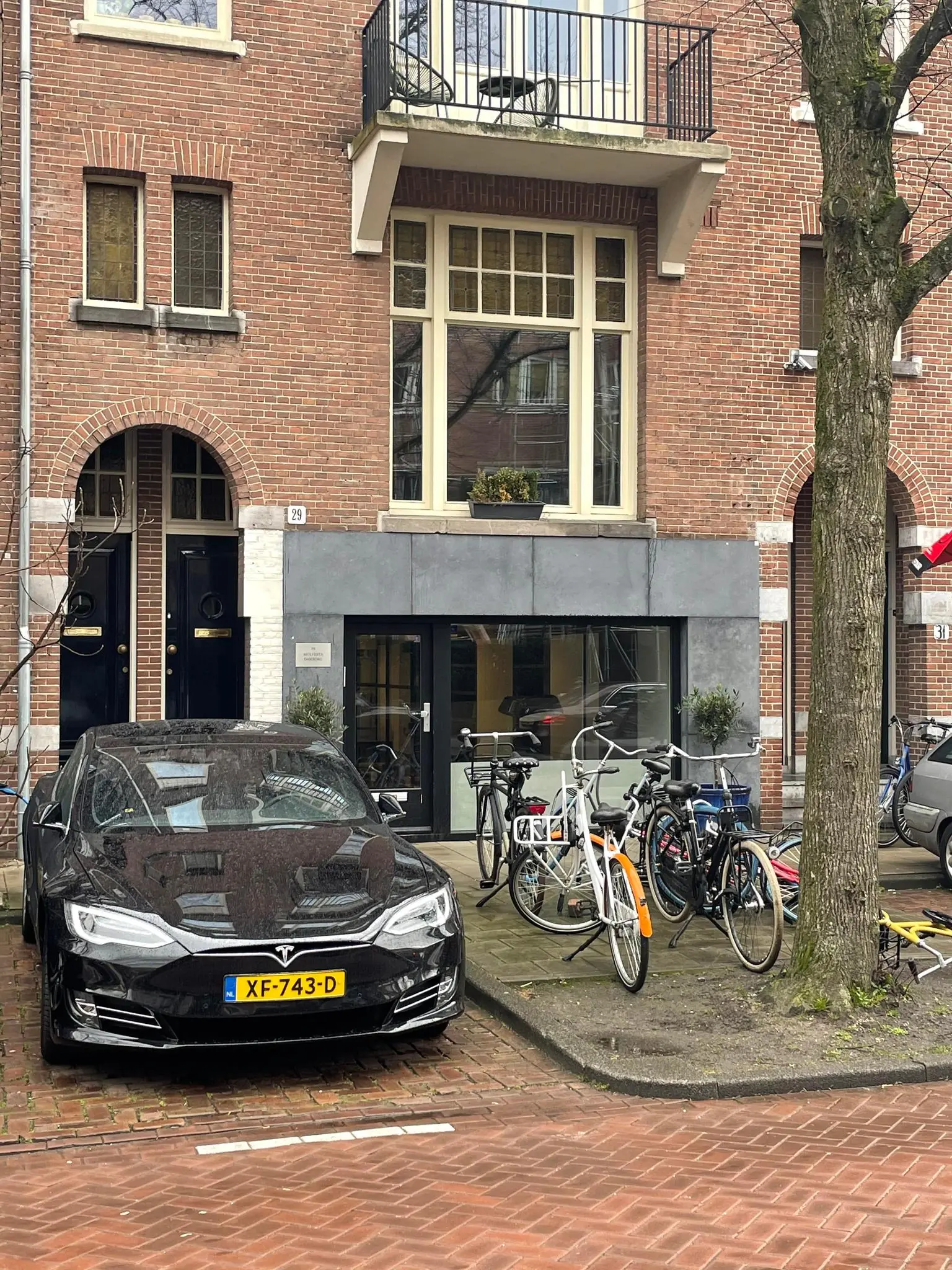 Een zwarte Tesla en meerdere fietsen geparkeerd voor een bakstenen gebouw aan de Emmastraat.