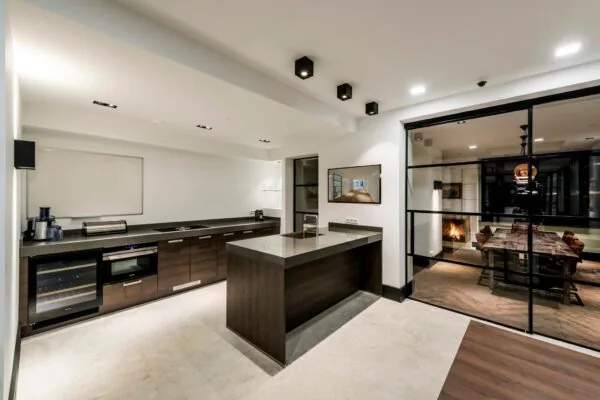 Moderne keuken met donker houten kasten en kookeiland, grenzend aan een eetkamer met glazen schuifdeuren.