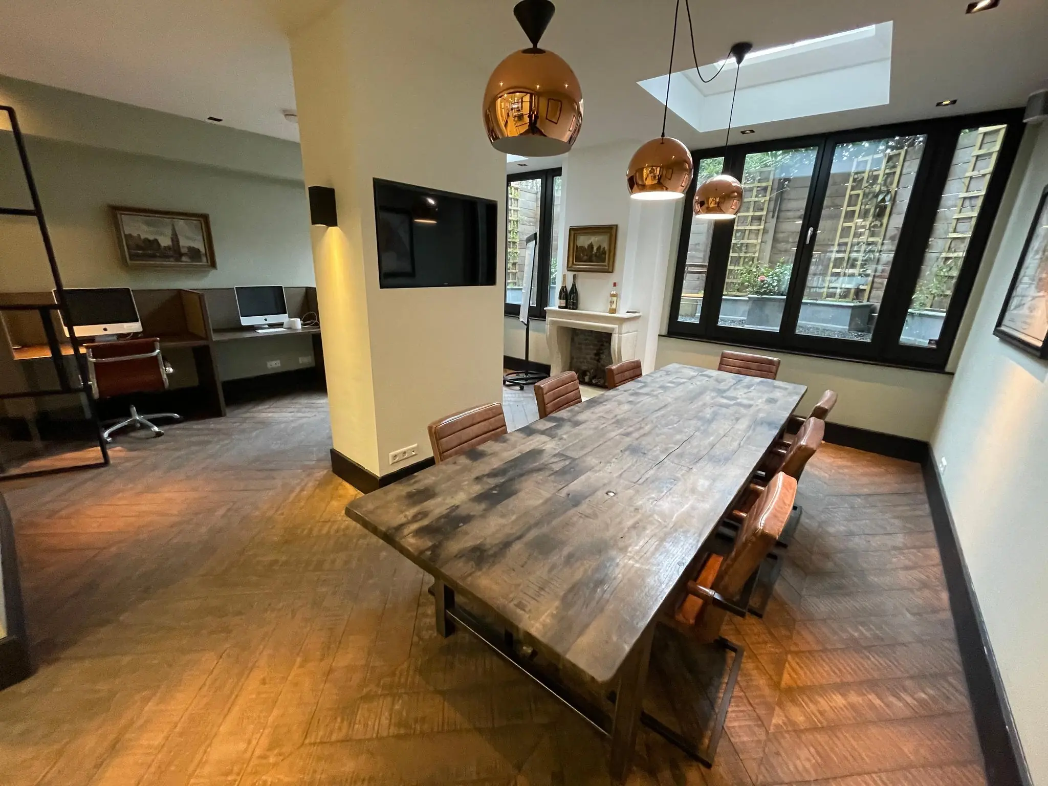 Vergaderruimte aan de Emmastraat met houten tafel, leren stoelen, hanglampen en aparte werkplekken met iMacs.
