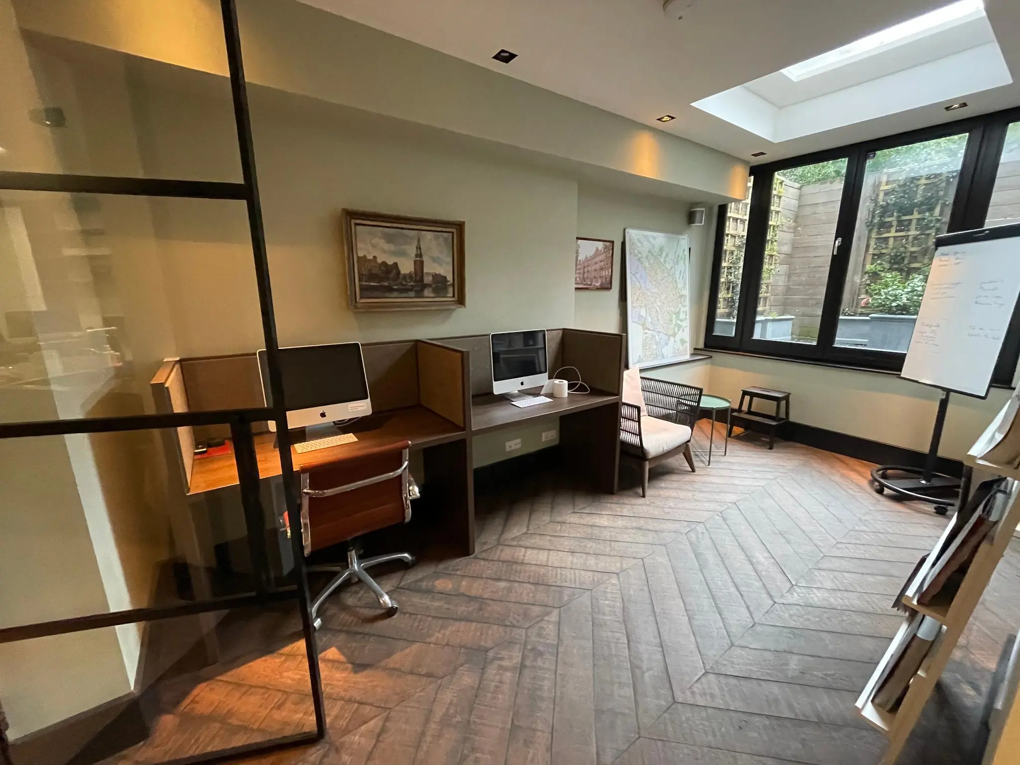 Moderne kantoorruimte aan de Emmastraat met werkplekken, een whiteboard en een grote raampartij met uitzicht op een binnentuin.