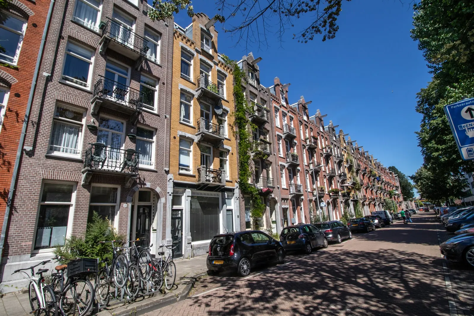 Rij karakteristieke Amsterdamse herenhuizen aan de Domselaerstraat op een zonnige dag.