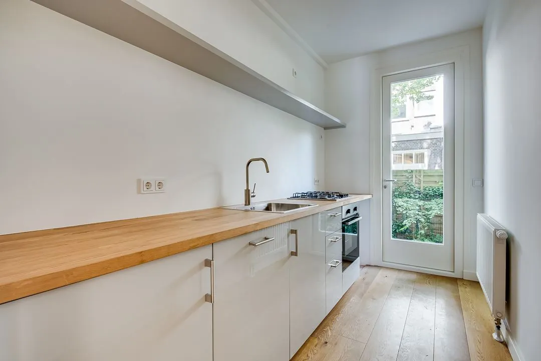 Moderne witte keuken in de Domselaerstraat met houten werkblad, ingebouwde oven en een deur naar de tuin.