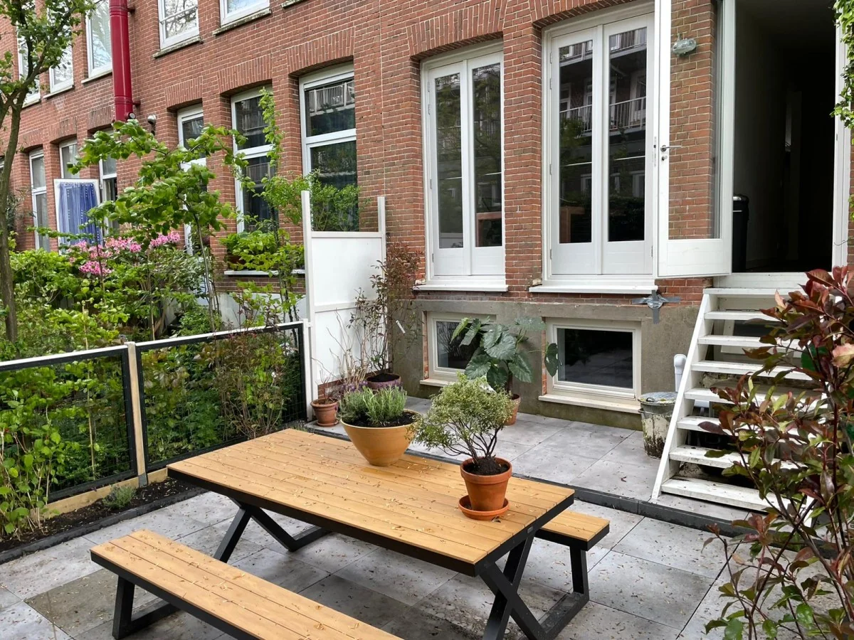 Binnentuin met houten picknicktafel en planten, grenzend aan een bakstenen woning aan de Domselaerstraat.