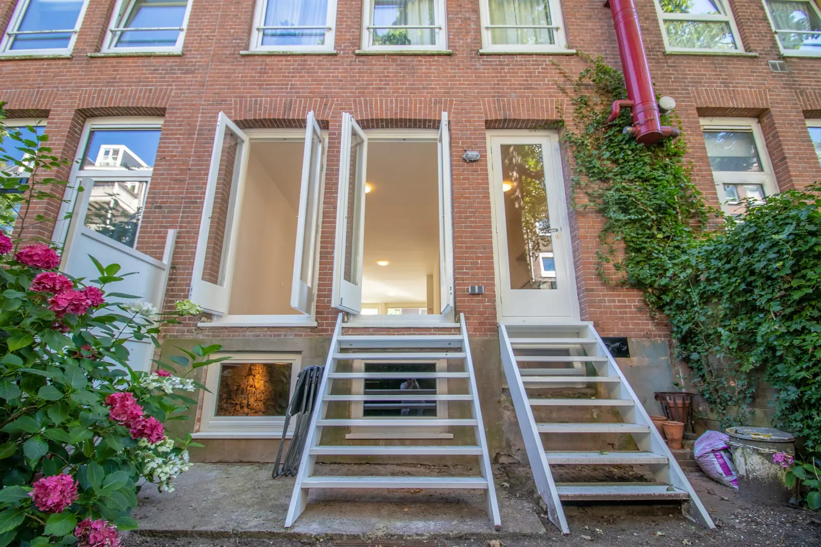 Achterzijde van een bakstenen woonhuis aan de Domselaerstraat met twee witte trappen naar openslaande deuren en zicht op een beganegrondverdieping.