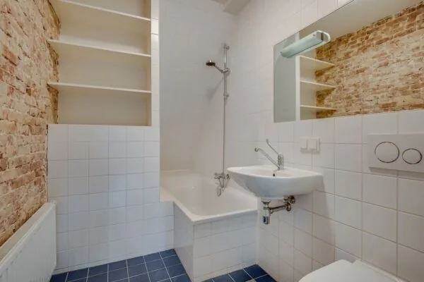 Moderne badkamer in de Domselaerstraat met wit tegelwerk, een bad met douche, wastafel, toilet en een muur met bakstenen.