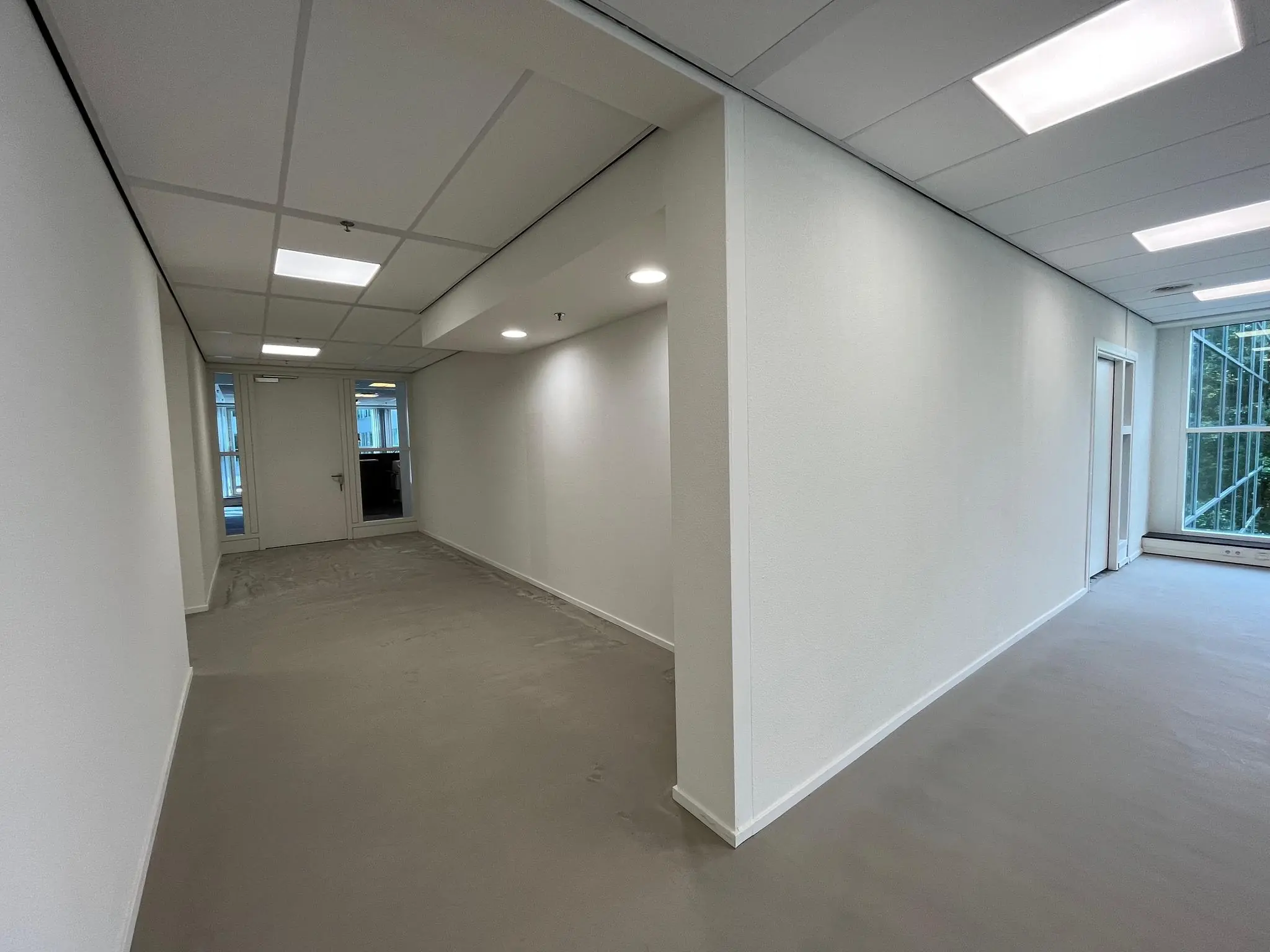 Gerenoveerde gang en kantoorruimte met witte muren en systeemplafond aan de Newtonlaan.