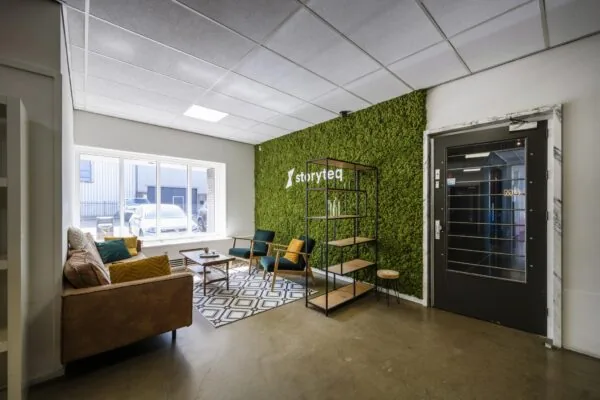 Wachtkamer met modern meubilair, groene moswand en het logo van Storyteq aan de Vliegtuigstraat.