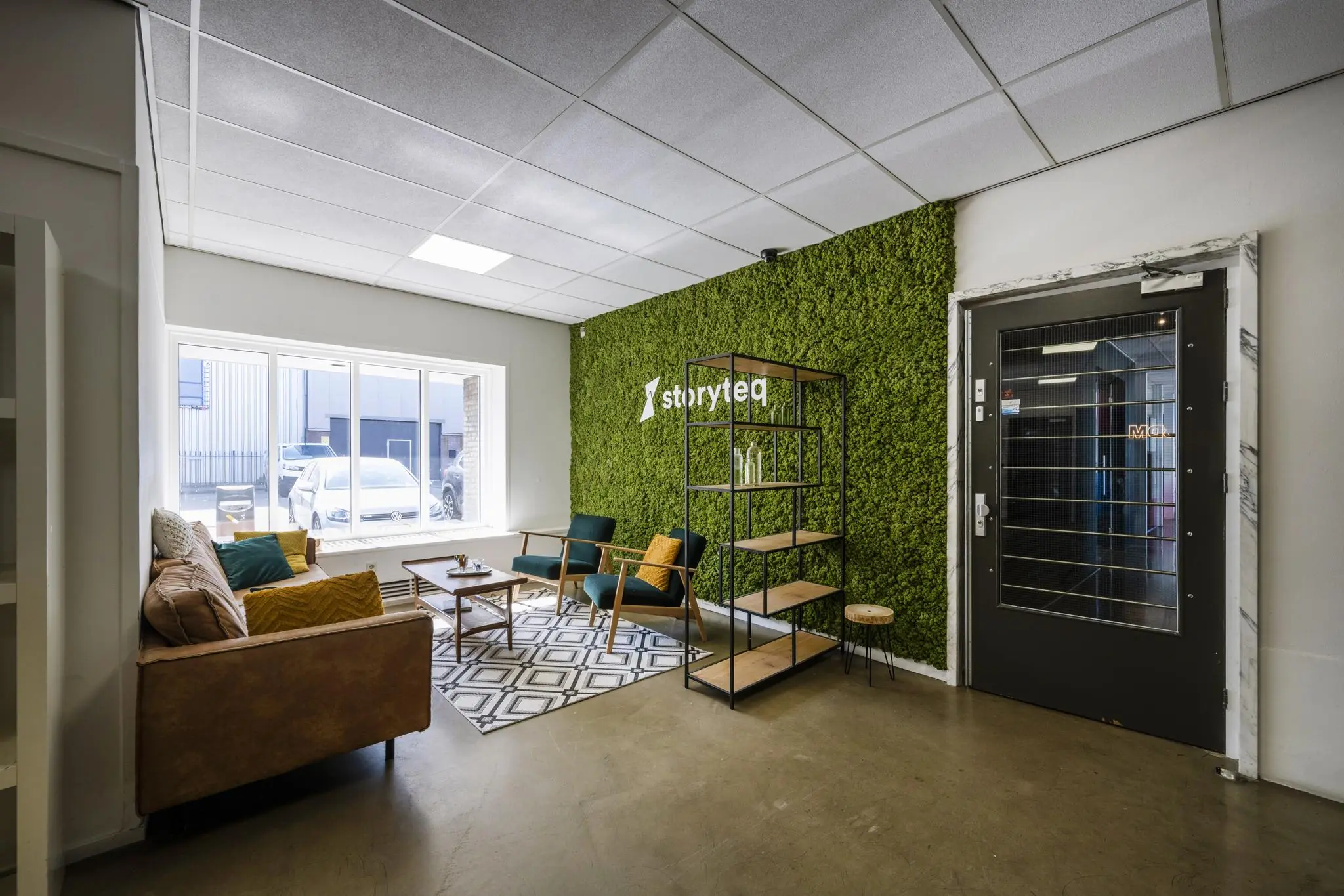 Wachtkamer met modern meubilair, groene moswand en het logo van Storyteq aan de Vliegtuigstraat.