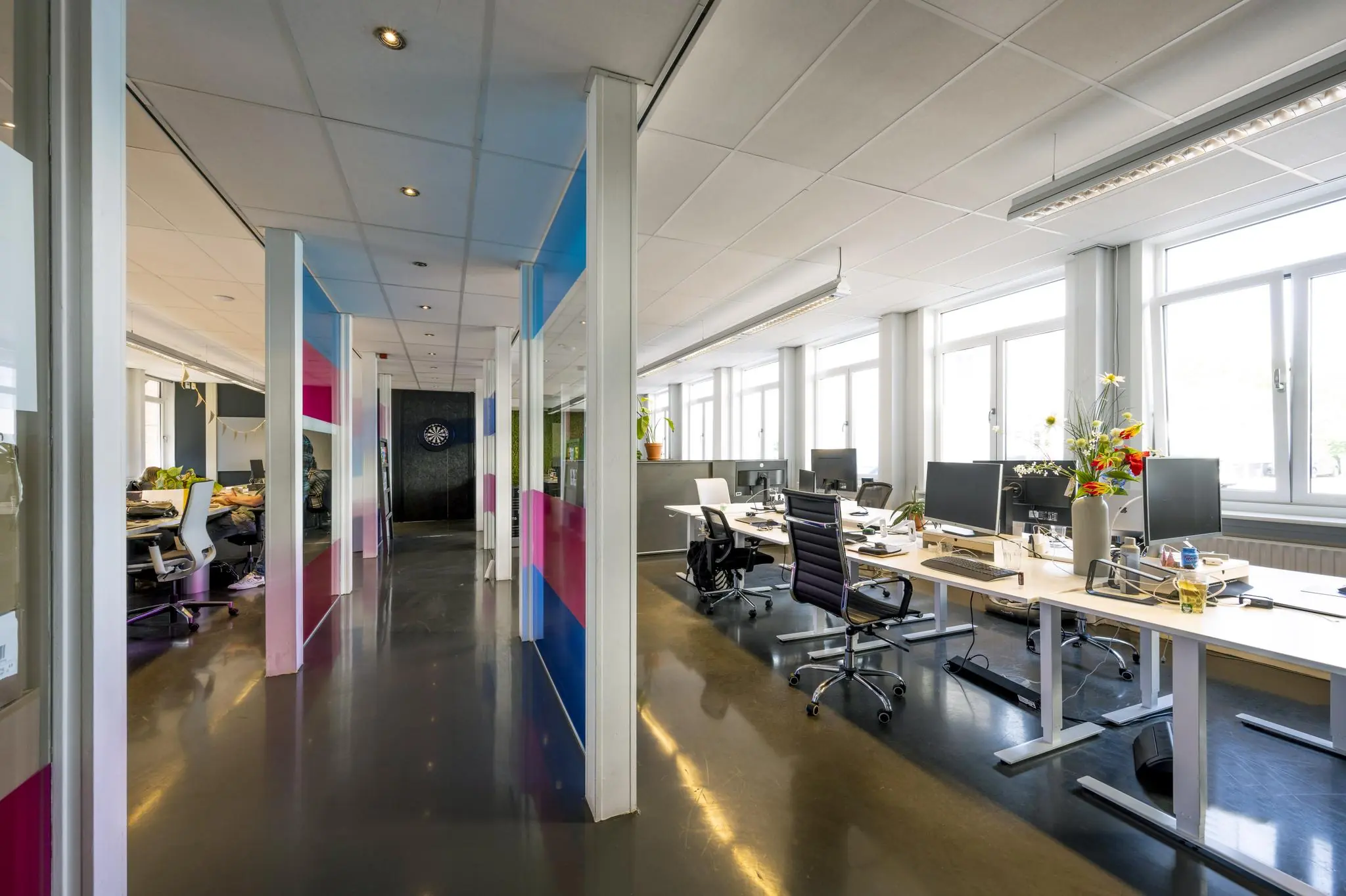 Modern kantoorinterieur aan de Vliegtuigstraat met open werkplekken, kleurrijke glazen wanden en veel daglicht.