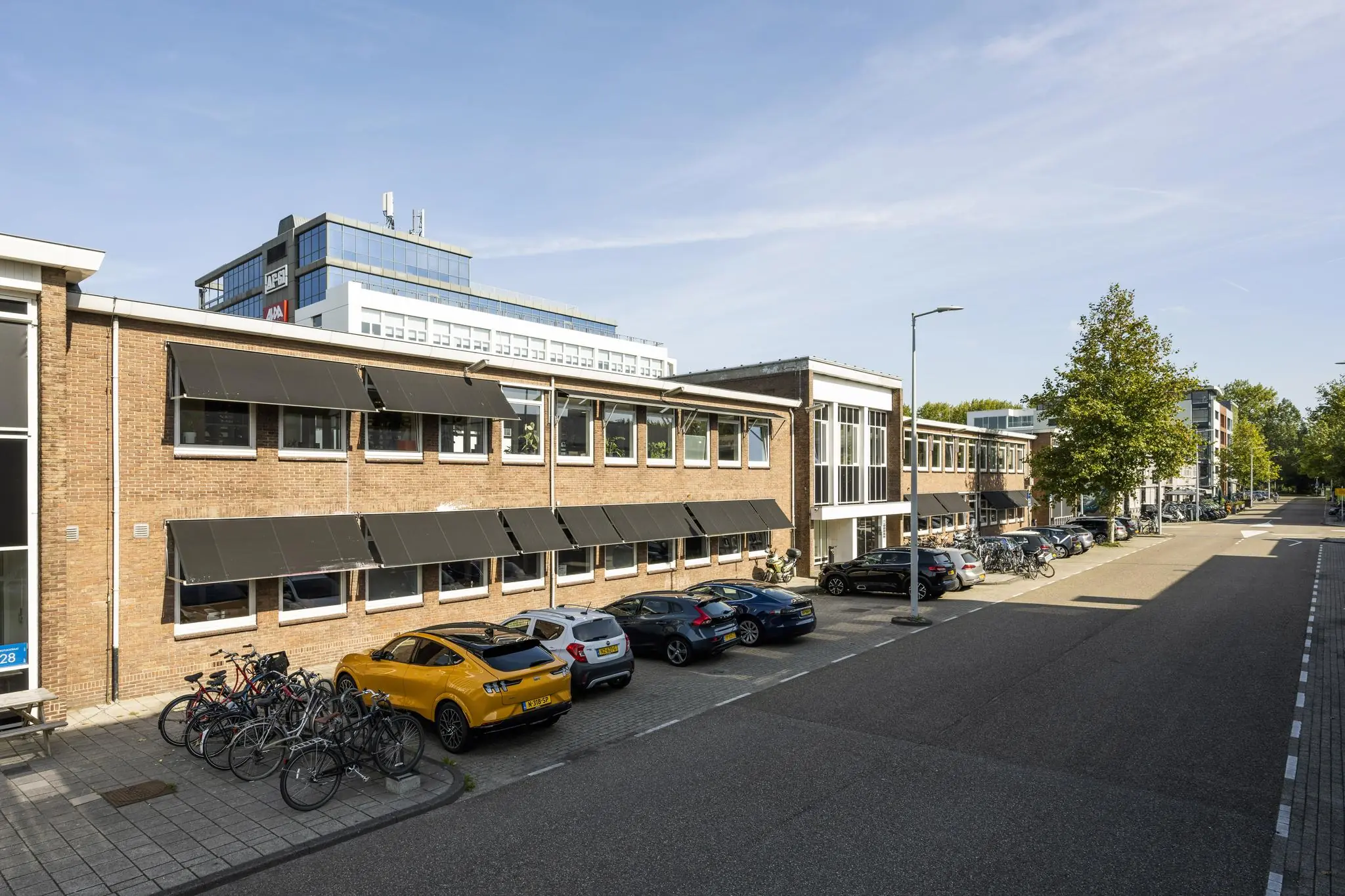 Straatbeeld van de Vliegtuigstraat met geparkeerde auto’s, fietsen en kantoorpanden op een zonnige dag.