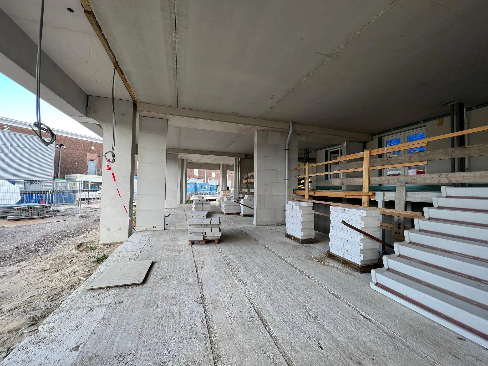 Bouwplaats aan de Cartesiusweg met gestapelde bouwmaterialen en een onafgebouwde betonnen constructie.