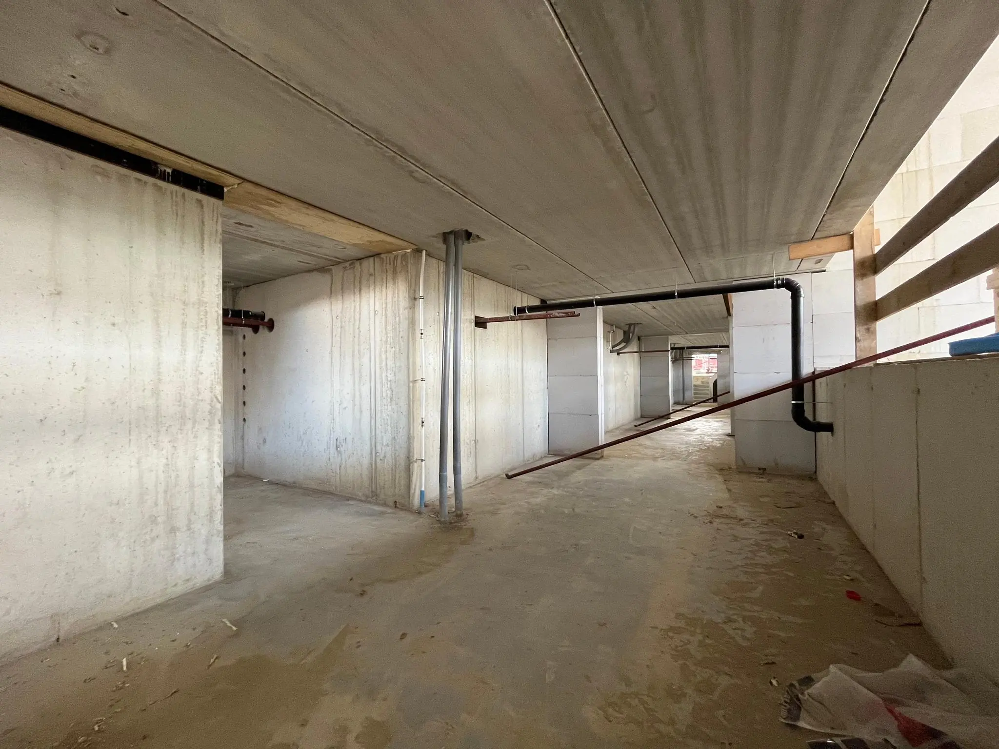 Ruwe betonnen gang in aanbouw aan de Cartesiusweg met zicht op leidingen en onafgewerkte muren.