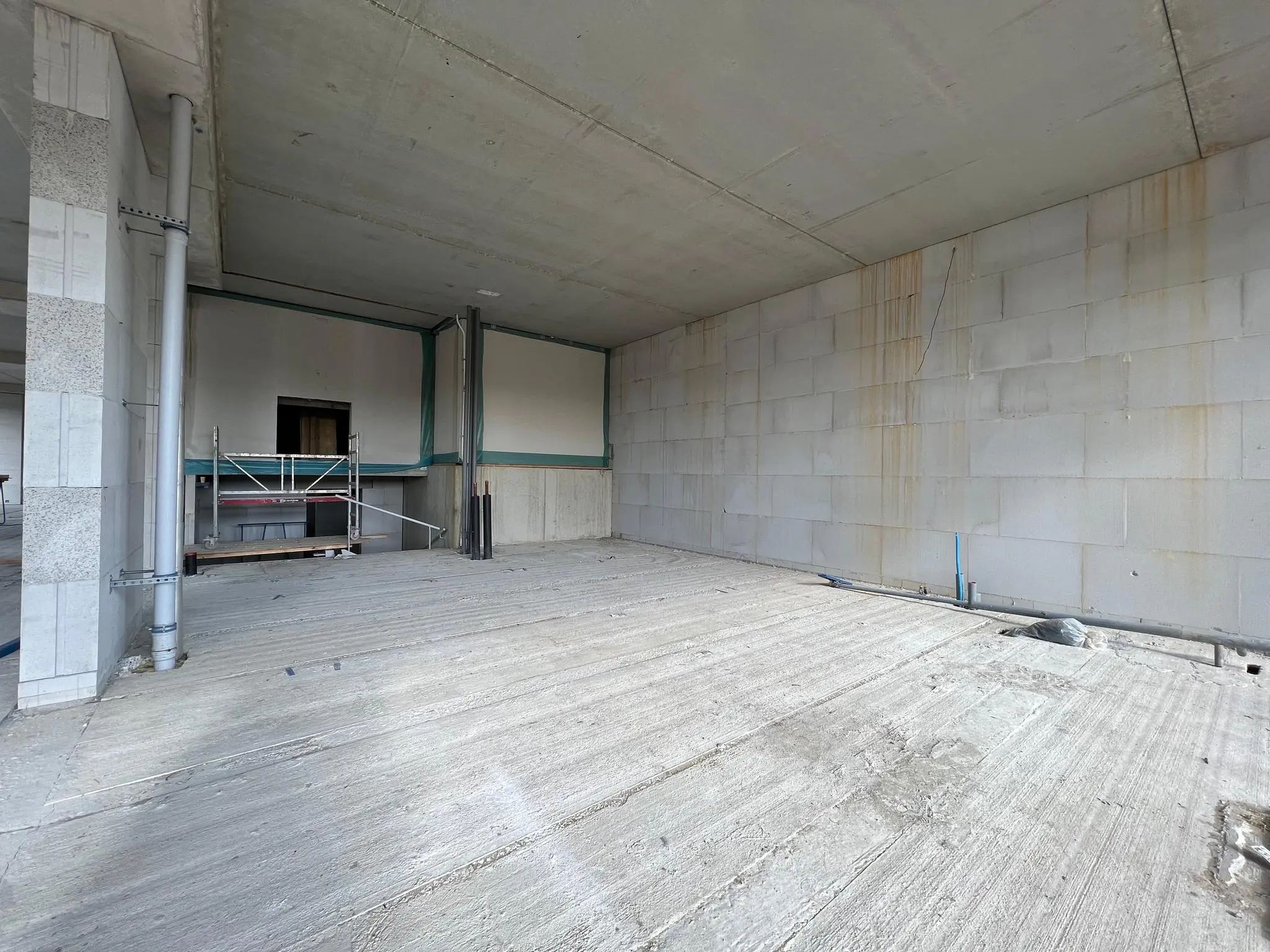 Een onafgewerkte ruimte in aanbouw aan de Cartesiusweg met betonnen vloer en zichtbare leidingen en steiger.