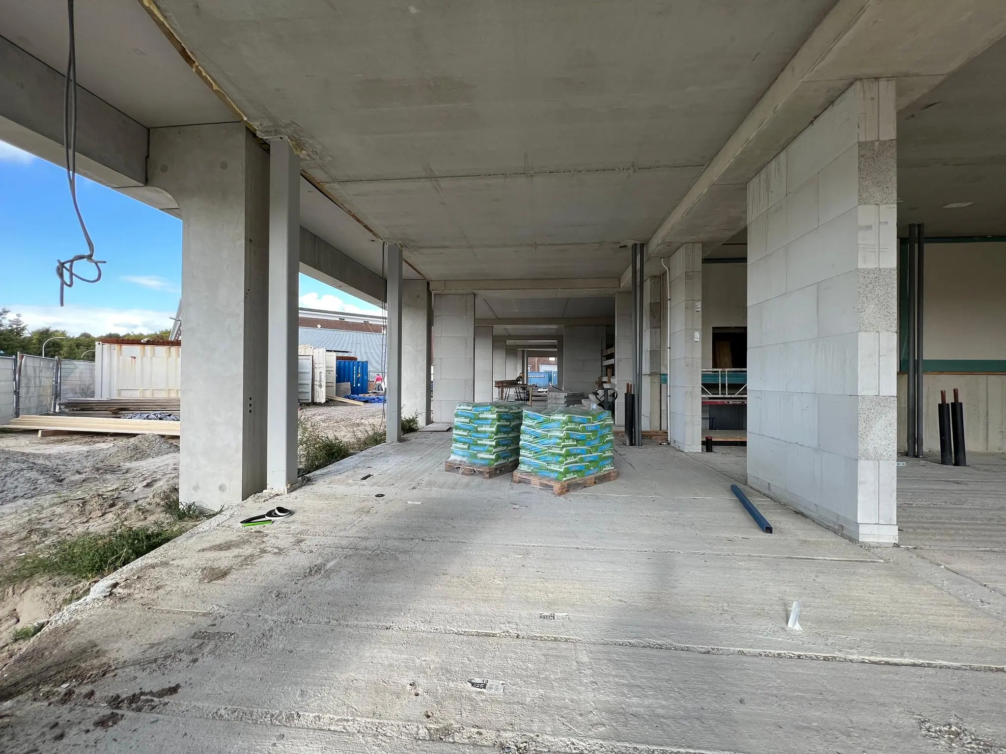 Een betonnen nieuwbouwconstructie aan de Cartesiusweg met stapels bouwmaterialen en zicht op de ruwbouw.