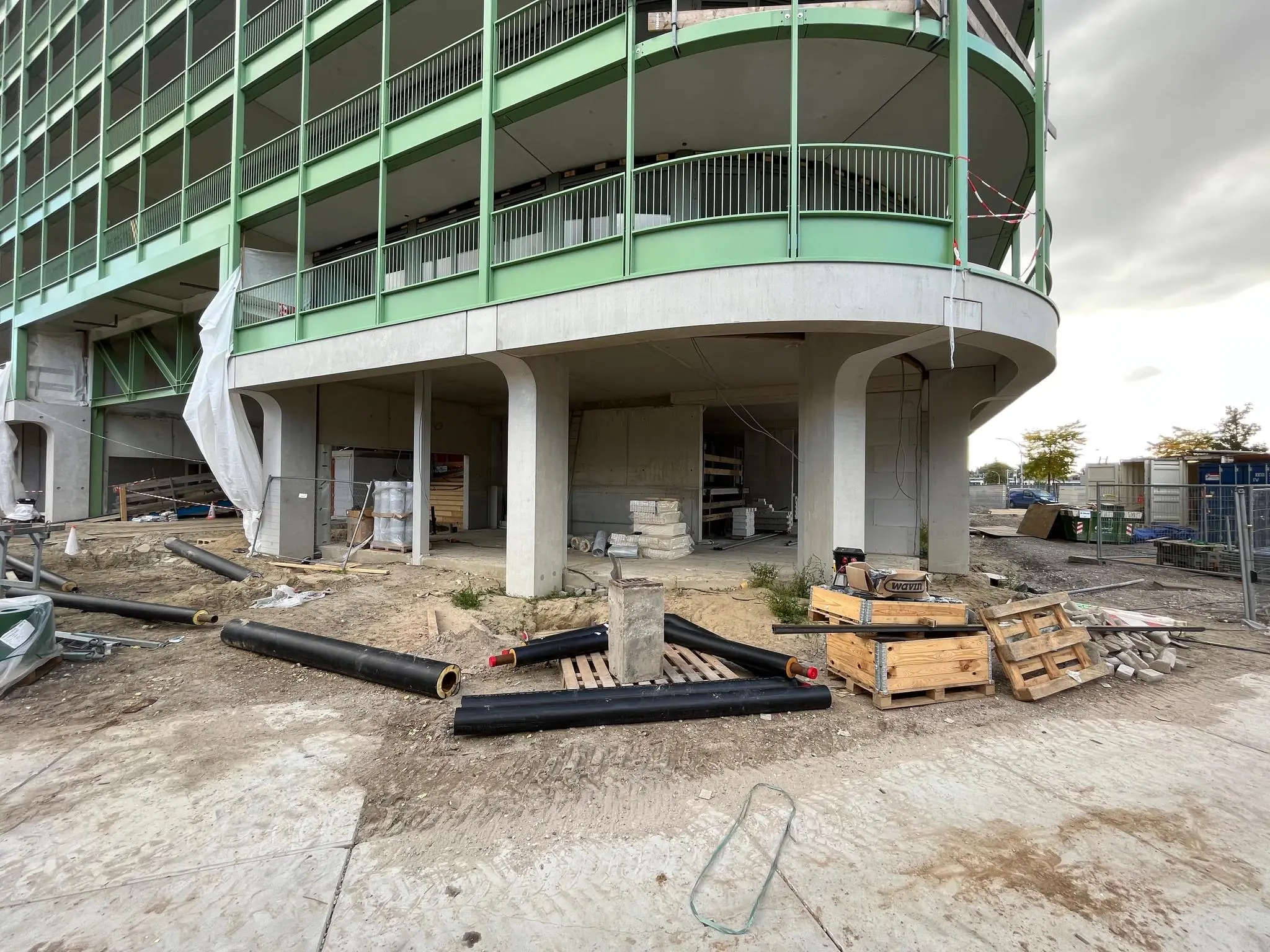Bouwplaats aan de Cartesiusweg met een deels afgerond groen gebouw en bouwmaterialen op de voorgrond.