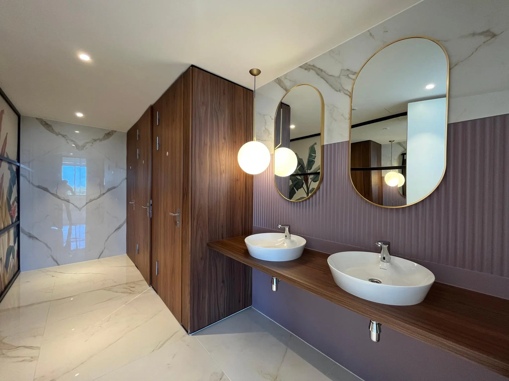 Moderne openbare toiletruimte aan de Europalaan met marmeren vloertegels, houten afwerking, twee wastafels en grote spiegels.