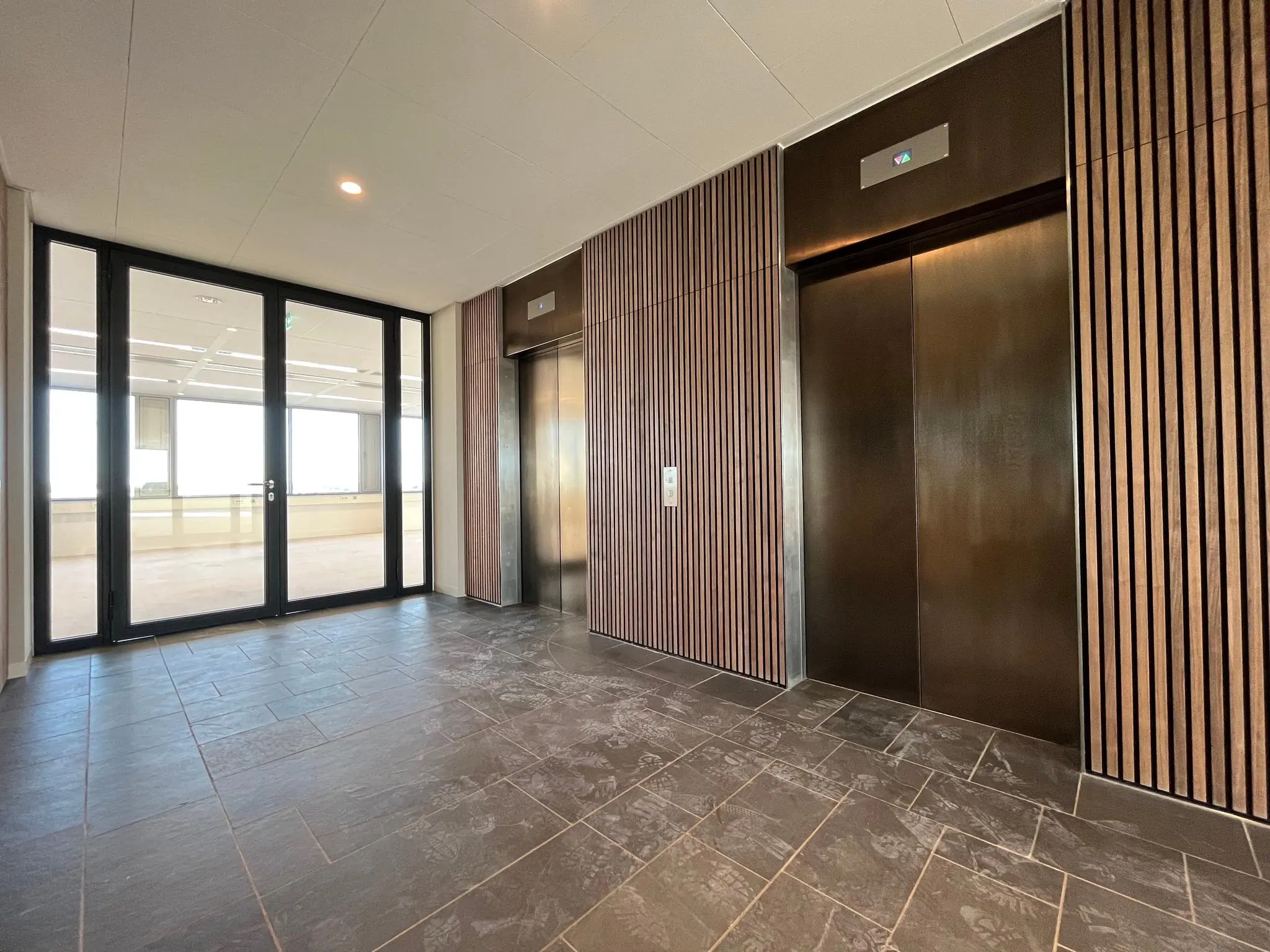 Modern ingerichte liftlobby in het kantoorgebouw aan de Europalaan met twee liften en grote glazen deuren naar een open ruimte.