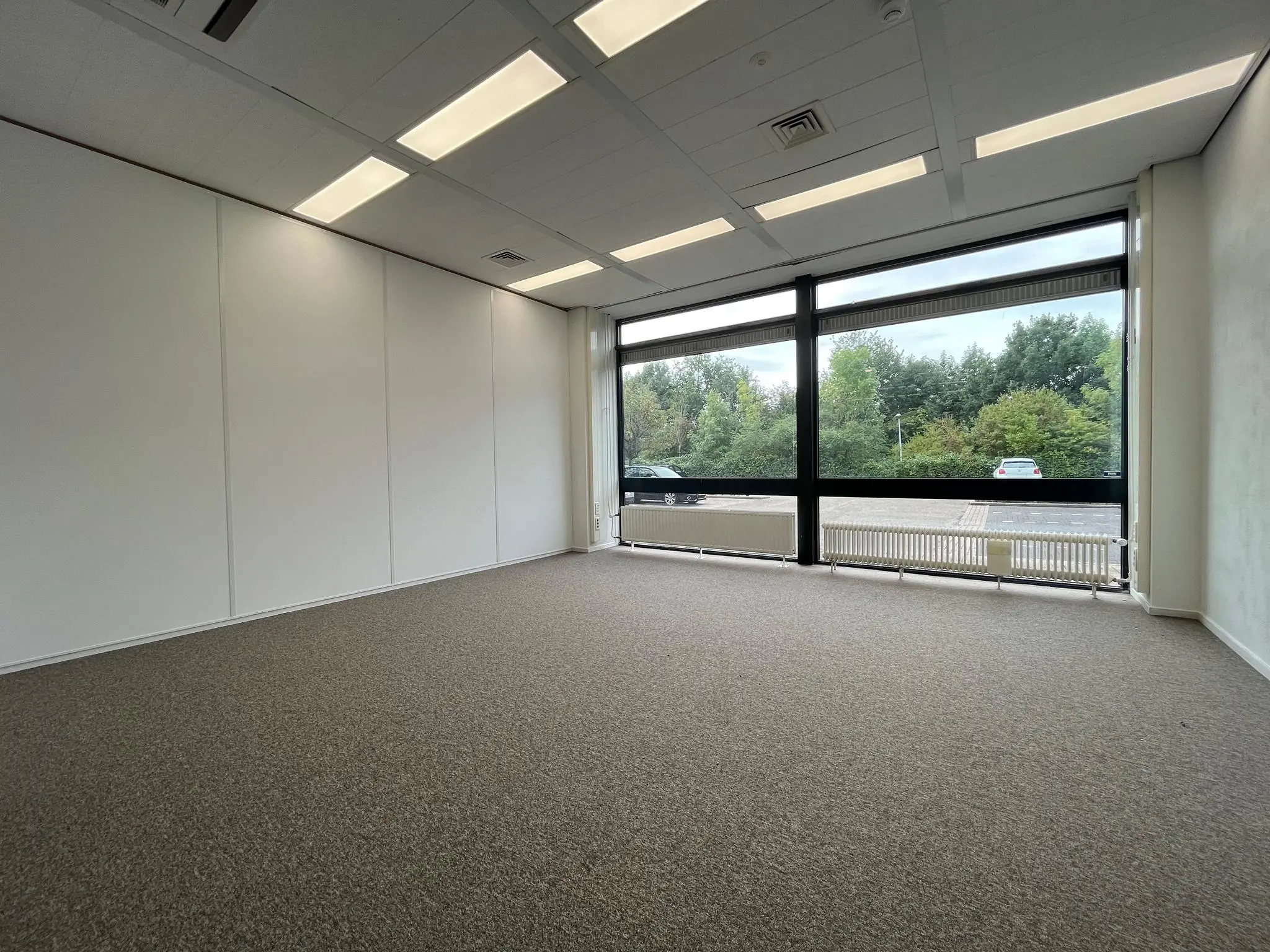 Leeg kantoorruimte aan de Zonnebaan met grote ramen en uitzicht op een parkeerplaats en groen.