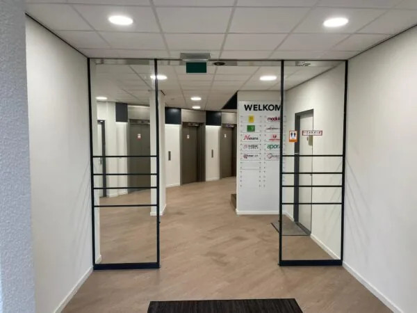 Ingang van een bedrijfsverzamelgebouw aan de Overschieseweg met zicht op een liftlobby en welkomstbord met bedrijfsnamen.