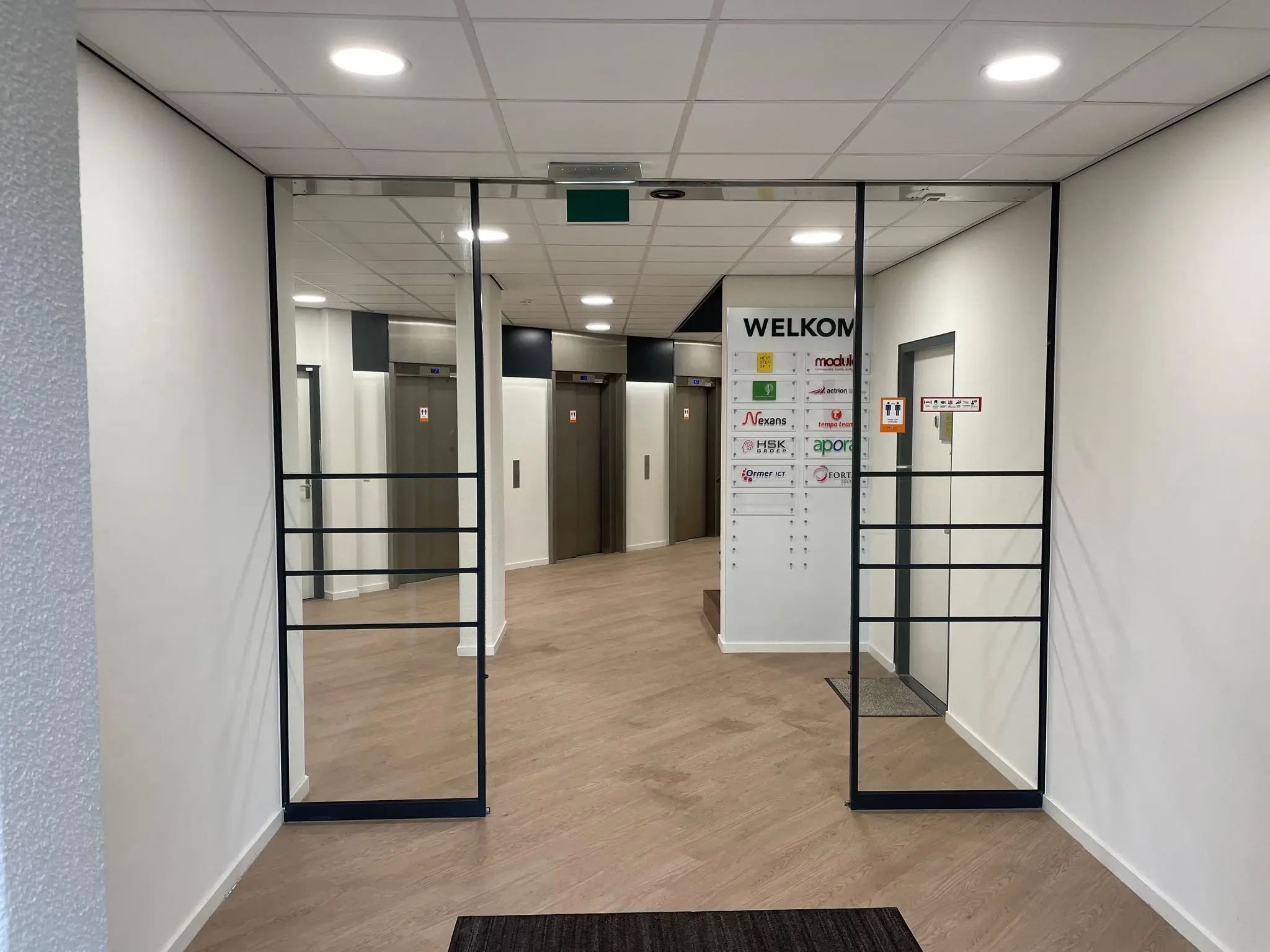 Ingang van een bedrijfsverzamelgebouw aan de Overschieseweg met zicht op een liftlobby en welkomstbord met bedrijfsnamen.