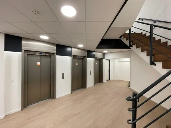 Moderne hal met drie liften en een houten trap aan de Overschieseweg.