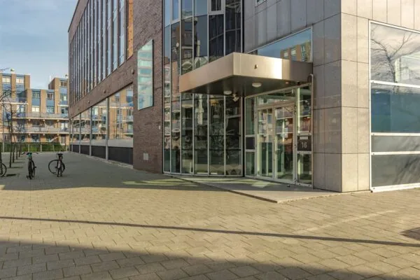 Ingang van een modern kantoorgebouw aan de Dynamostraat met glazen entree en fietsen op de voorgrond.