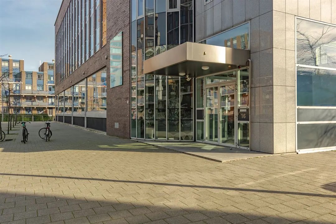 Ingang van een modern kantoorgebouw aan de Dynamostraat met glazen entree en fietsen op de voorgrond.