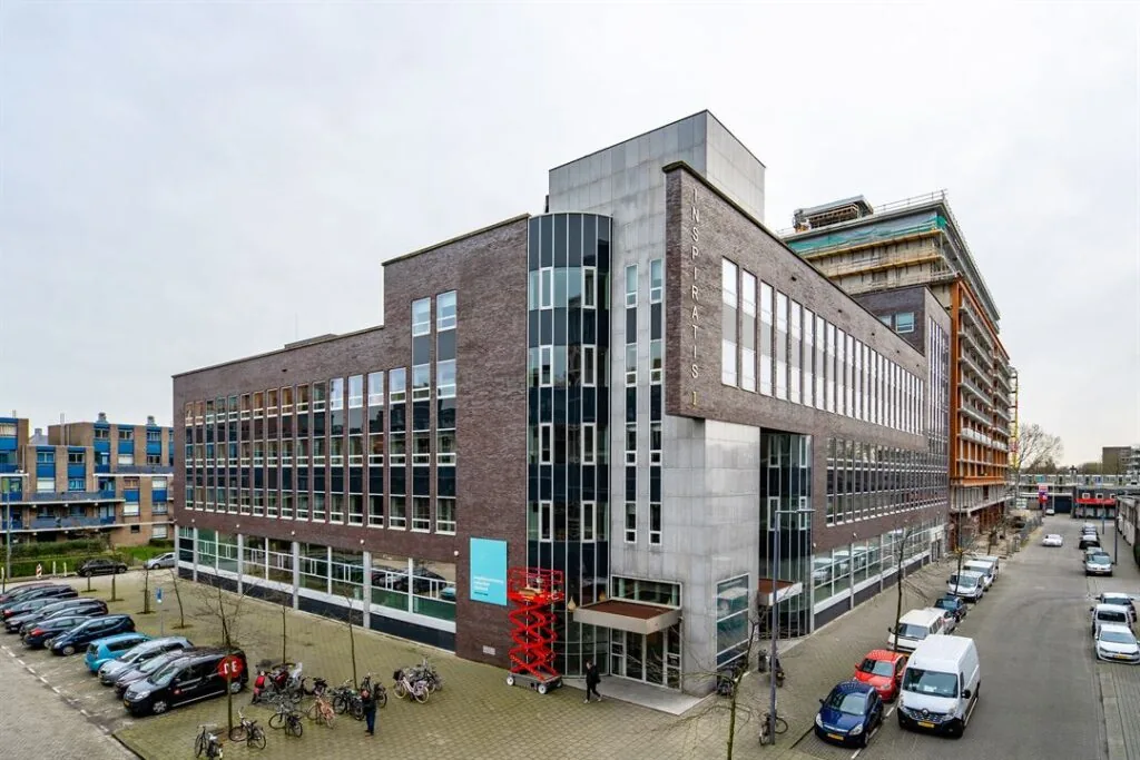 Kantoorgebouw aan de Dynamostraat met moderne gevel en geparkeerde auto’s en fietsen op de voorgrond.