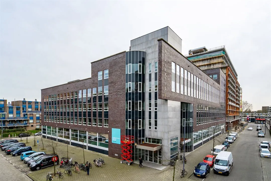 Kantoorgebouw aan de Dynamostraat met moderne gevel en geparkeerde auto’s en fietsen op de voorgrond.