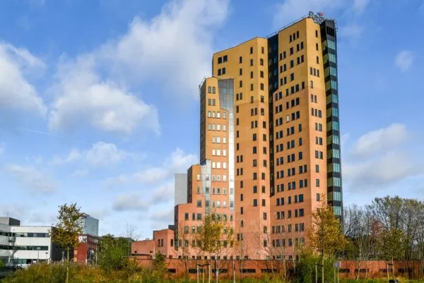 Hoog kantoorgebouw aan de Kingsfordweg in Amsterdam met oranje en bruine gevels tegen een blauwe lucht.