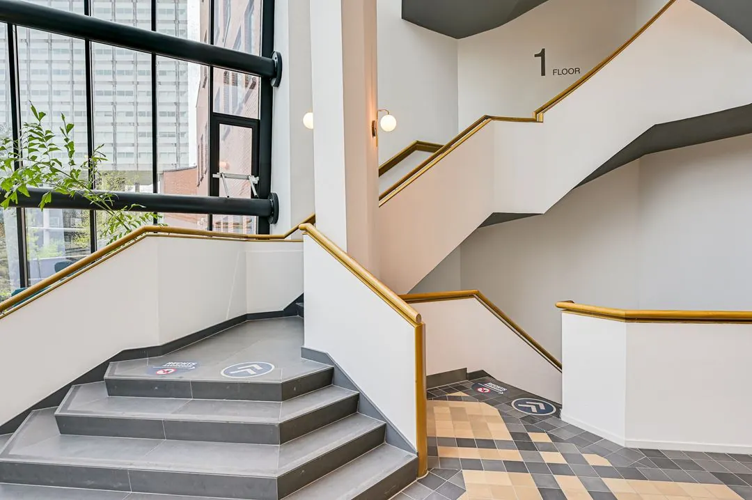 Moderne binnentrap met houten leuningen in een kantoorgebouw aan de Kingsfordweg, met zicht op grote ramen en etage-aanduiding.