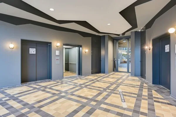 Moderne liftlobby aan de Kingsfordweg met drie liften, geometrisch plafondontwerp en betegelde vloer.