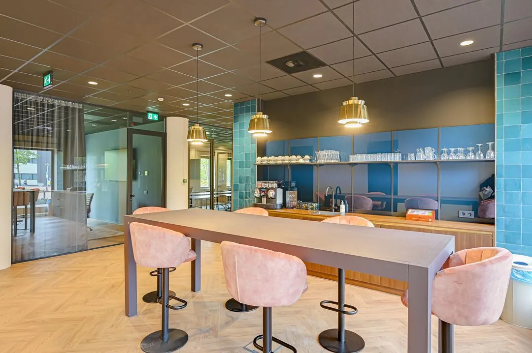 Moderne bedrijfskeuken met een hoge tafel, roze stoelen en een koffiehoek aan de Kingsfordweg.