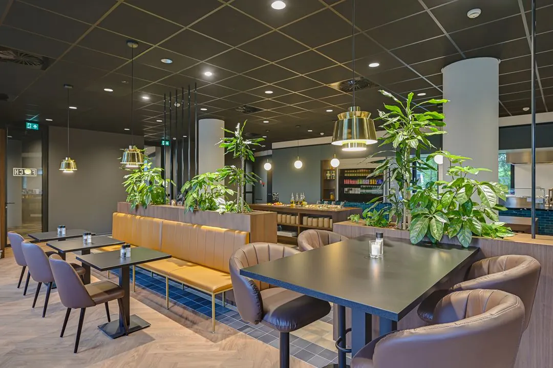 Modern en sfeervol ingericht bedrijfsrestaurant aan de Kingsfordweg met zitplaatsen, groene planten en warme verlichting.