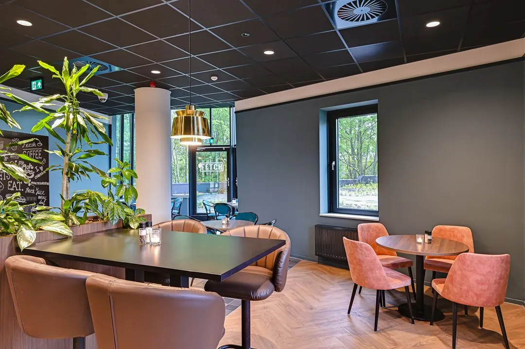 Modern ingerichte zithoek in een bedrijfsrestaurant aan de Kingsfordweg met planten, kleurrijke stoelen en grote ramen.