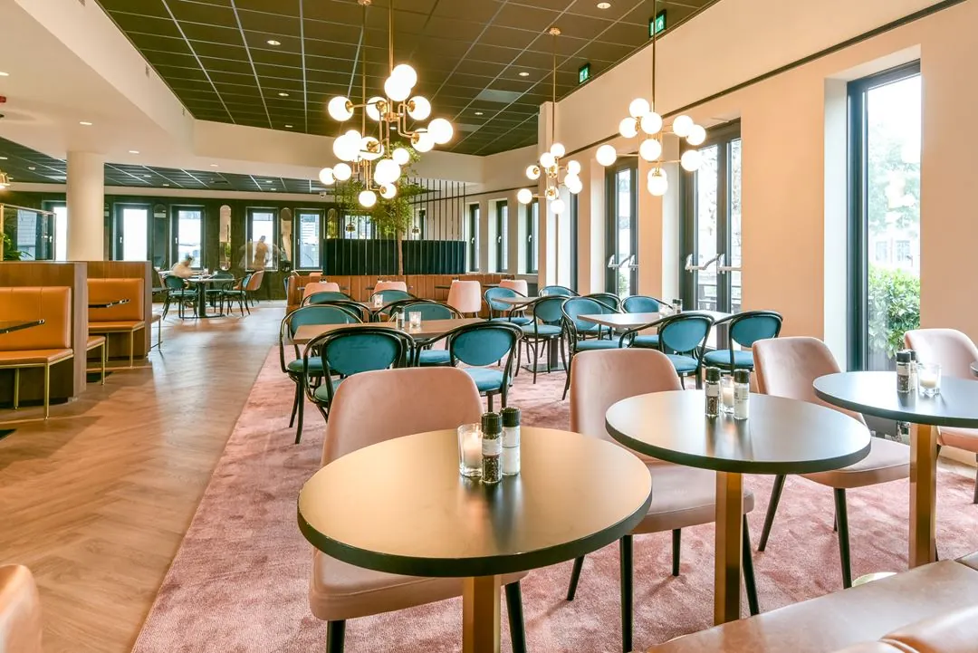 Modern ingerichte eetruimte aan de Kingsfordweg met ronde tafels, fluwelen stoelen en opvallende hanglampen.