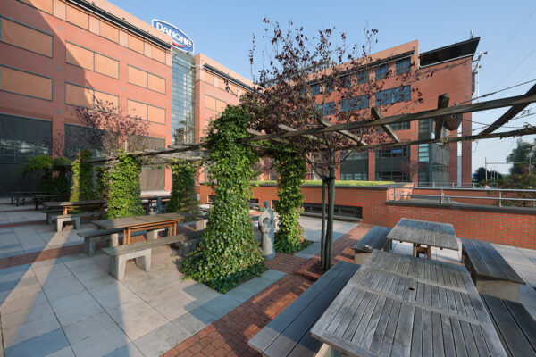 Buiten zitgedeelte met houten picknicktafels en begroeide pergola's bij het Danone-kantoor aan de Zonnebaan.
