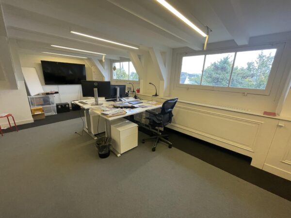 Modern kantoorinterieur aan de Herengracht met bureaus, computerschermen en een groot raam met uitzicht op bomen.