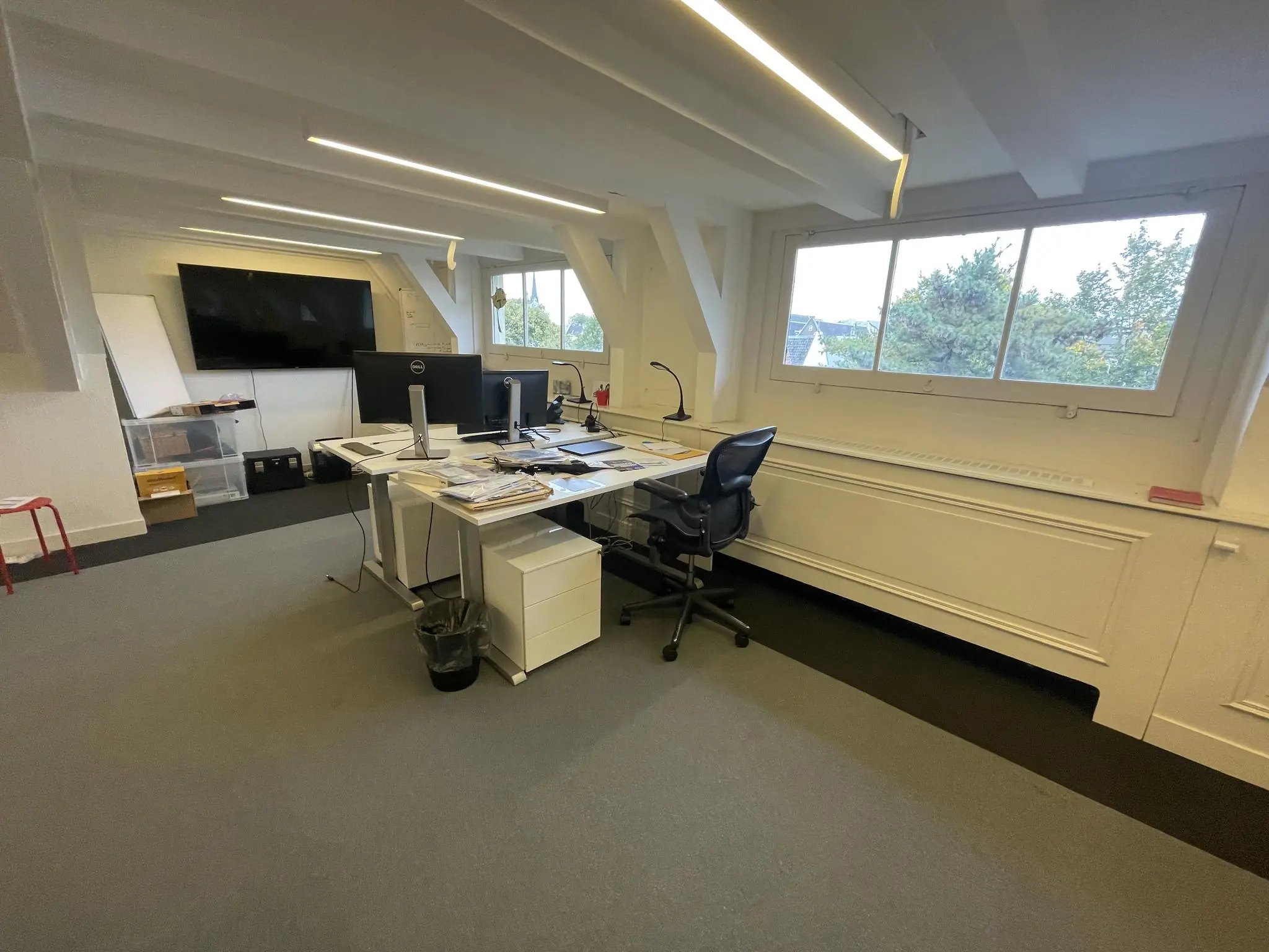 Modern kantoorinterieur aan de Herengracht met bureaus, computerschermen en een groot raam met uitzicht op bomen.