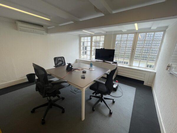 Vergaderruimte aan de Herengracht met een tafel, vier bureaustoelen, een tv-scherm en grote ramen met uitzicht op dakpannen.