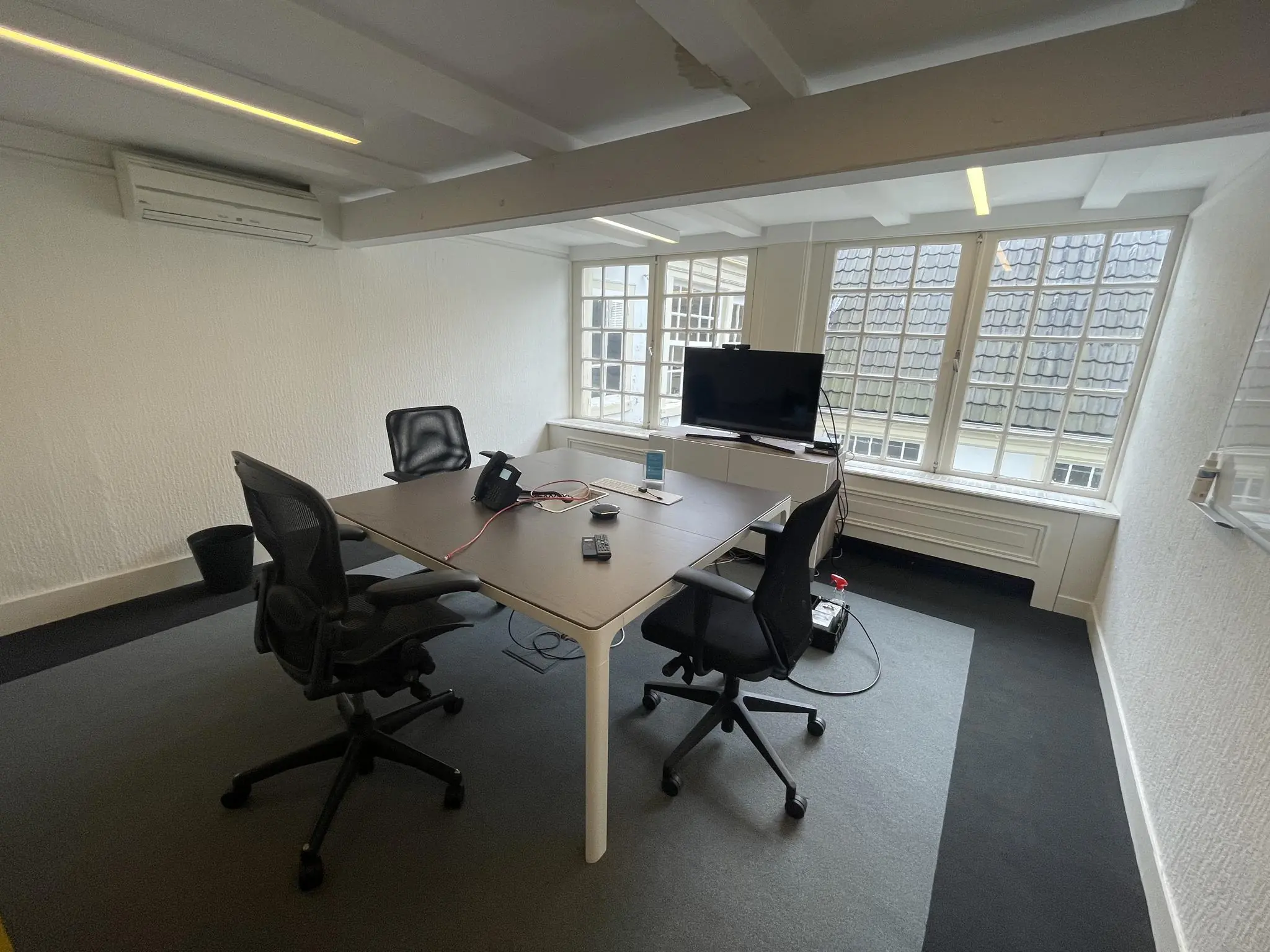 Vergaderruimte aan de Herengracht met een tafel, vier bureaustoelen, een tv-scherm en grote ramen met uitzicht op dakpannen.