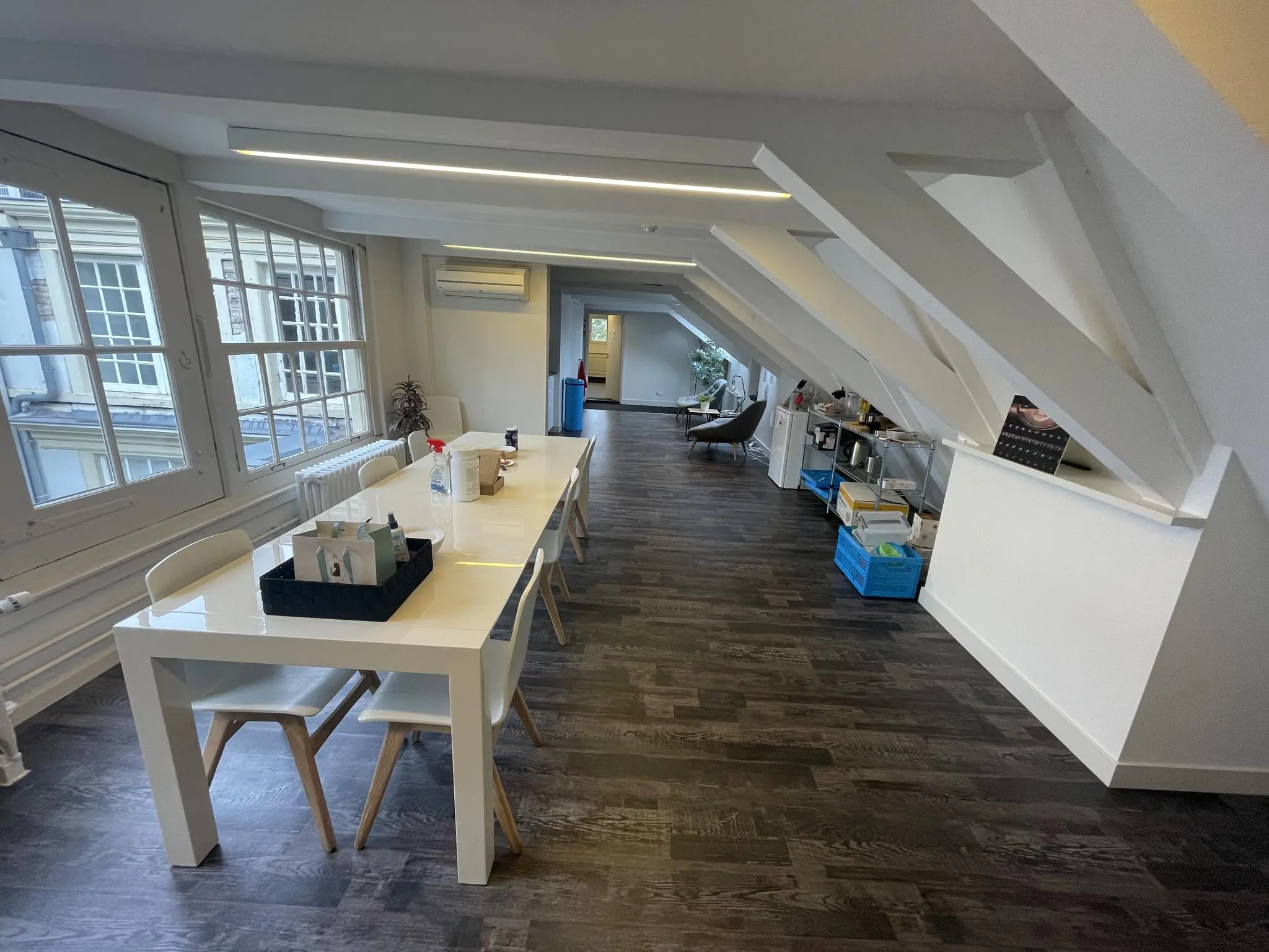 Moderne kantoorruimte aan de Herengracht met schuine plafonds, een lange witte tafel en grote ramen met uitzicht op klassieke gevels.