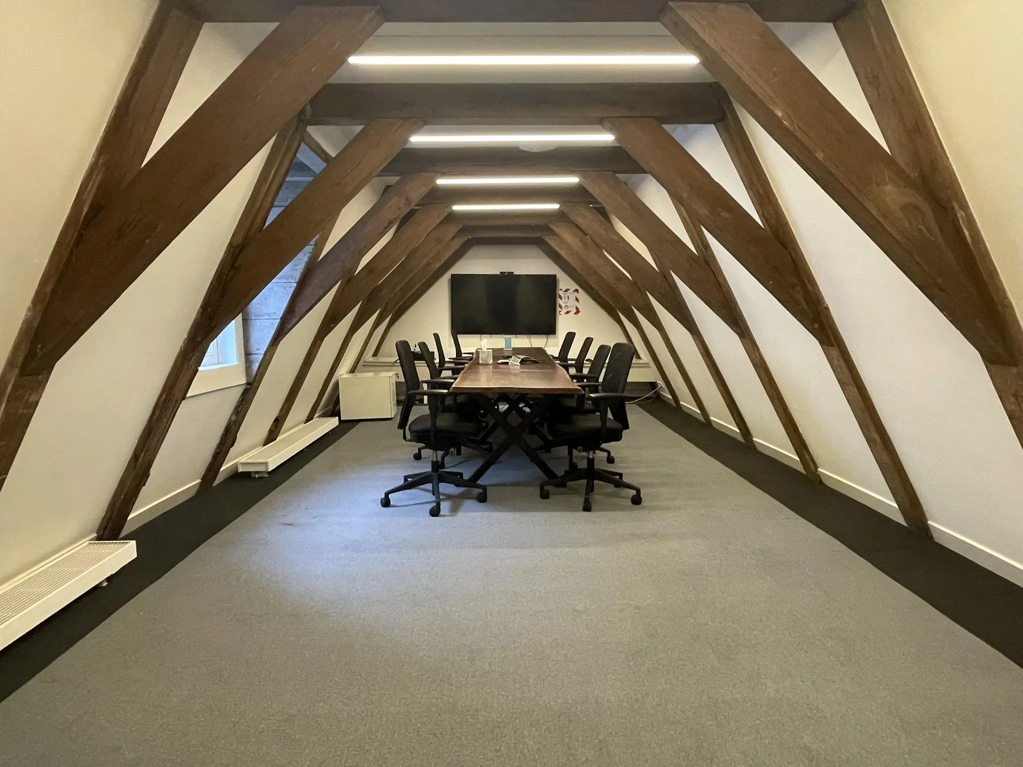 Vergaderruimte met houten balken, een lange tafel, bureaustoelen en een scherm aan de Herengracht.