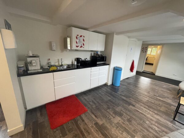 Keukenruimte aan de Herengracht met witte kasten, koffiezetapparaat, magnetron en blauwe afvalbak.