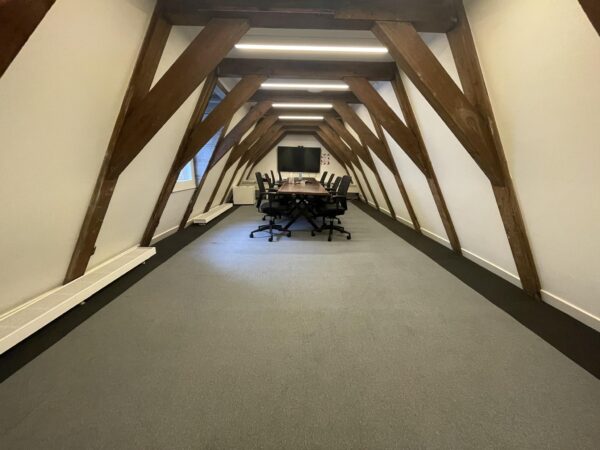 Vergaderzaal met houten balken, een lange tafel en bureaustoelen in een ruimte aan de Herengracht.