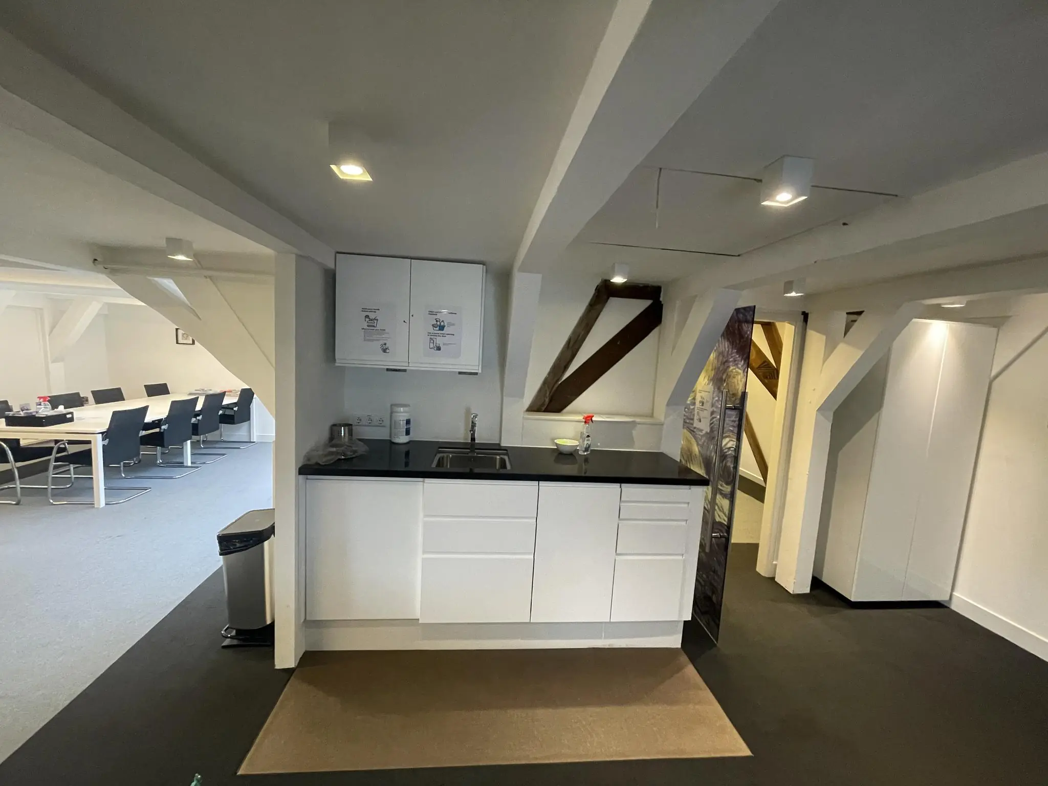 Kleine kitchenette met witte kasten in een modern kantoorpand aan de Herengracht, met vergaderruimte op de achtergrond.