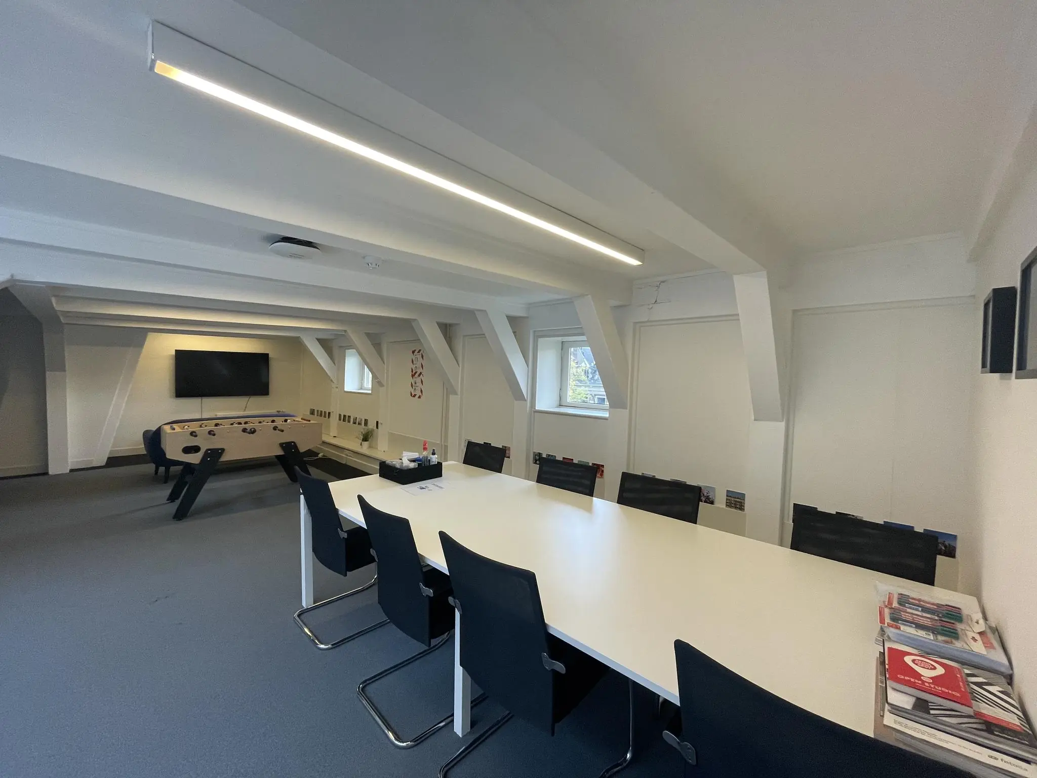 Vergaderruimte aan de Herengracht met een lange witte tafel, zwarte stoelen, een tafelvoetbaltafel en een tv-scherm.