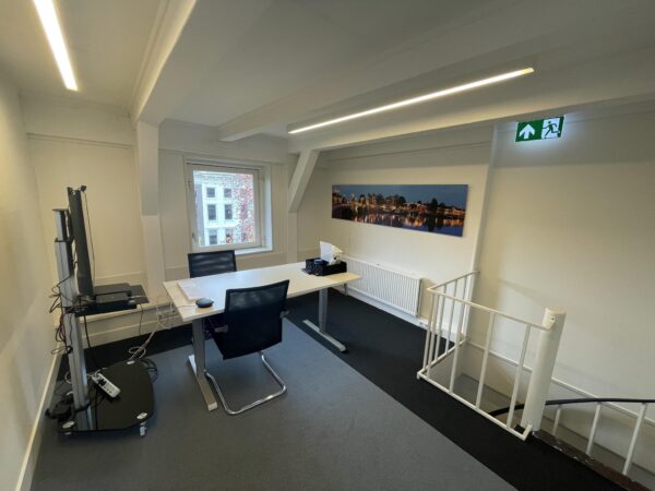 Modern kantoor met bureau, stoelen en computer, gelegen aan de Herengracht met uitzicht op een grachtenpand en een foto van Amsterdam aan de muur.