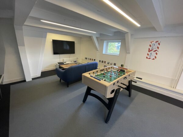 Recreatieruimte aan de Herengracht met een tafelvoetbaltafel, een bank en een televisie.