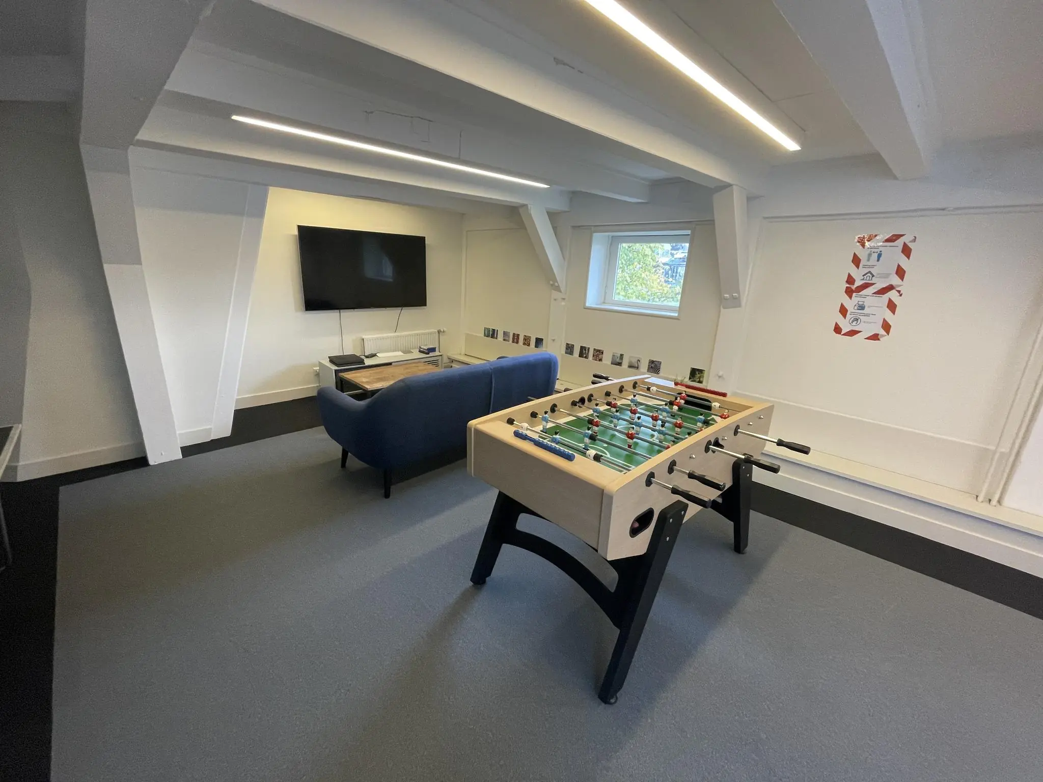 Recreatieruimte aan de Herengracht met een tafelvoetbaltafel, een bank en een televisie.